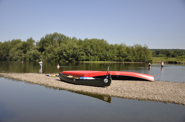 Canoes pulled up on the shingle bank with swimmers in the river