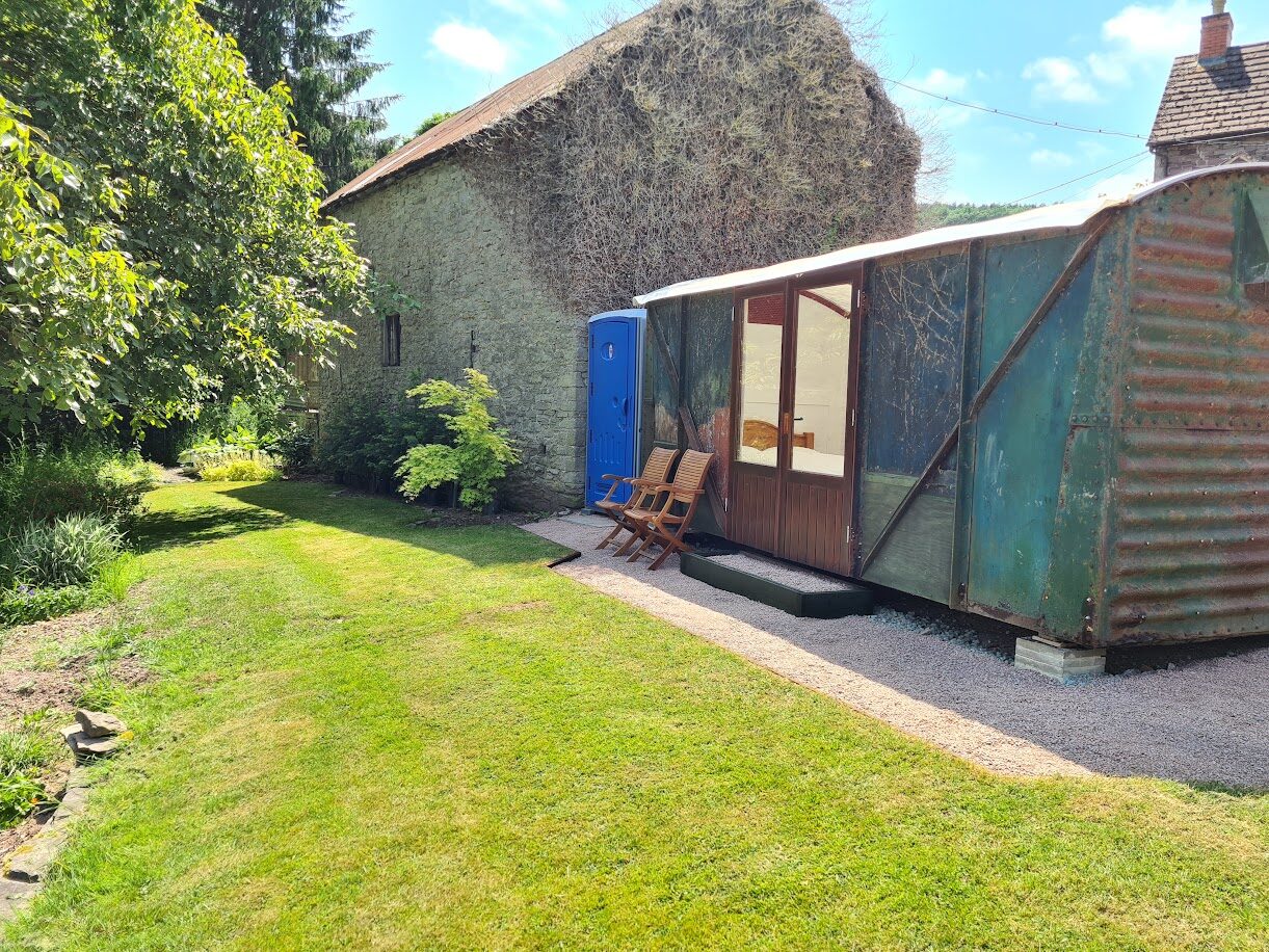 The restored railway wagon beside the stone barn, chairs on the gravel outside